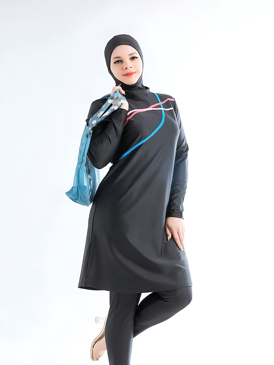 Une femme portant un hijab et un maillot de bain musulman noir avec des détails de couleur. Elle tient un sac de plage bleu.