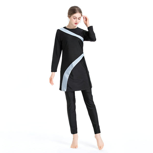 Une femme porte un maillot de bain musulman noir avec des détails gris. Le maillot de bain est à manches longues et comprend un pantalon long.