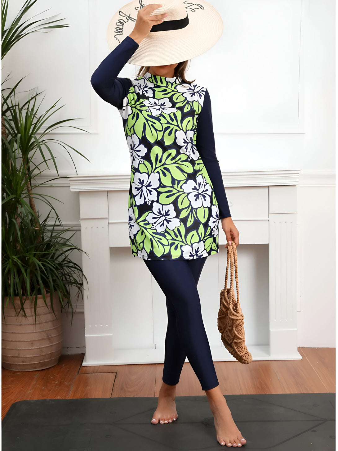 Une femme portant un maillot de bain musulman à manches longues avec un motif floral vert et blanc. Elle porte un chapeau de paille et un sac à main en osier.