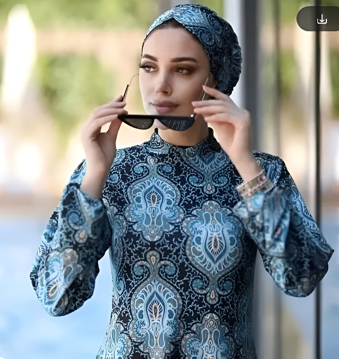 Une femme portant un hijab et une robe longue à motifs bleus et noirs. Elle porte des lunettes de soleil. La robe est idéale pour la mode musulmane.