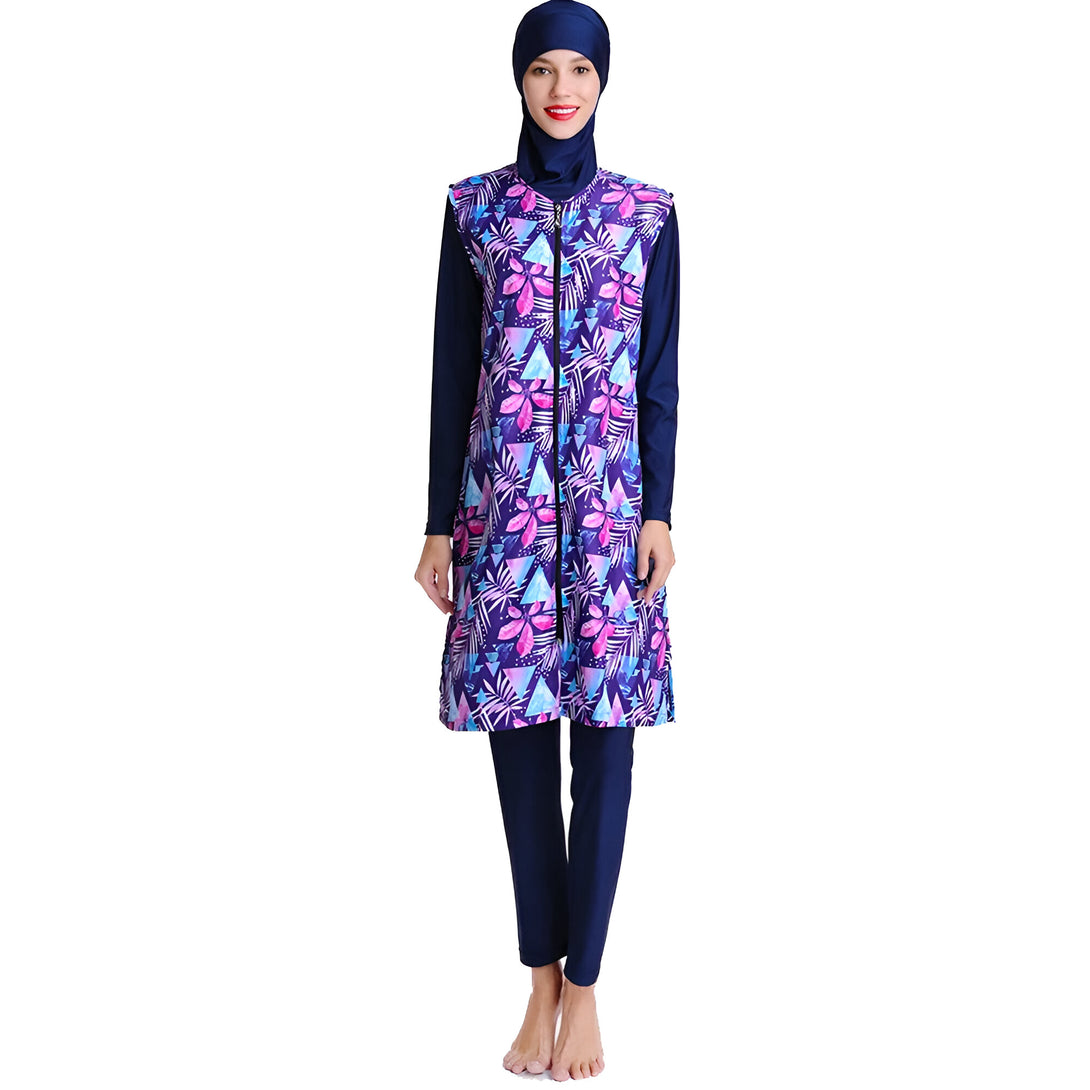 Une femme portant un maillot de bain musulman bleu foncé avec un imprimé floral bleu, rose et violet. Le maillot de bain a des manches longues et une fermeture éclair sur le devant. La femme porte également un hijab bleu foncé.