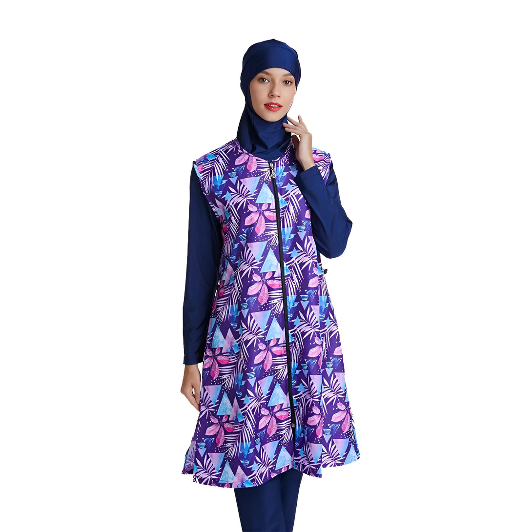 Une femme portant un maillot de bain islamique bleu marine et violet à imprimé floral.  Le maillot de bain a une fermeture éclair sur le devant et des manches longues. La femme porte également un hijab bleu marine.