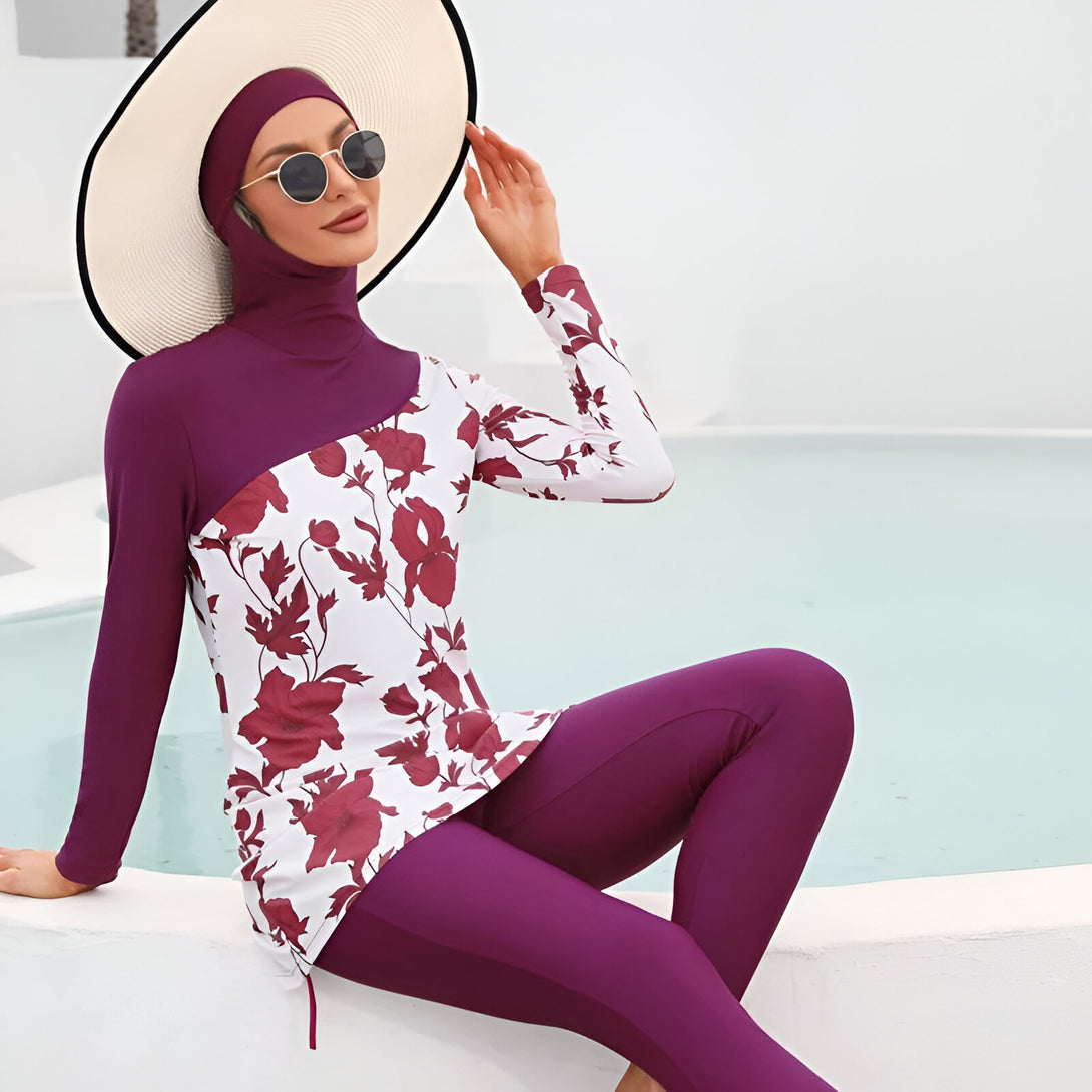 Une femme portant un maillot de bain musulman avec un motif floral rouge et blanc, un hijab violet et un chapeau de paille.