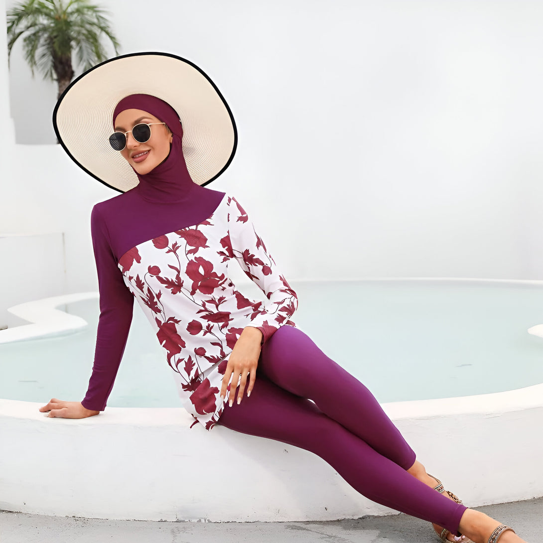 Une femme portant un maillot de bain musulman violet à fleurs, un chapeau de paille et des lunettes de soleil, assise près d'une piscine.