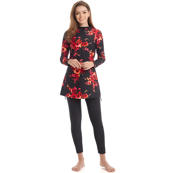 Une femme porte un maillot de bain musulman noir à fleurs rouges. Le maillot de bain a des manches longues et une jupe longue. La femme sourit à la caméra.