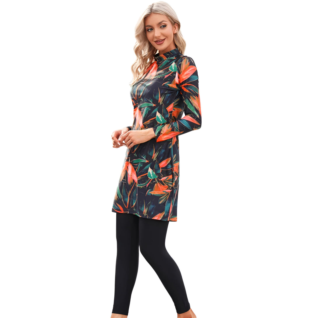 Une femme porte une robe longue à manches longues avec un motif floral orange et vert sur fond noir et un legging noir.