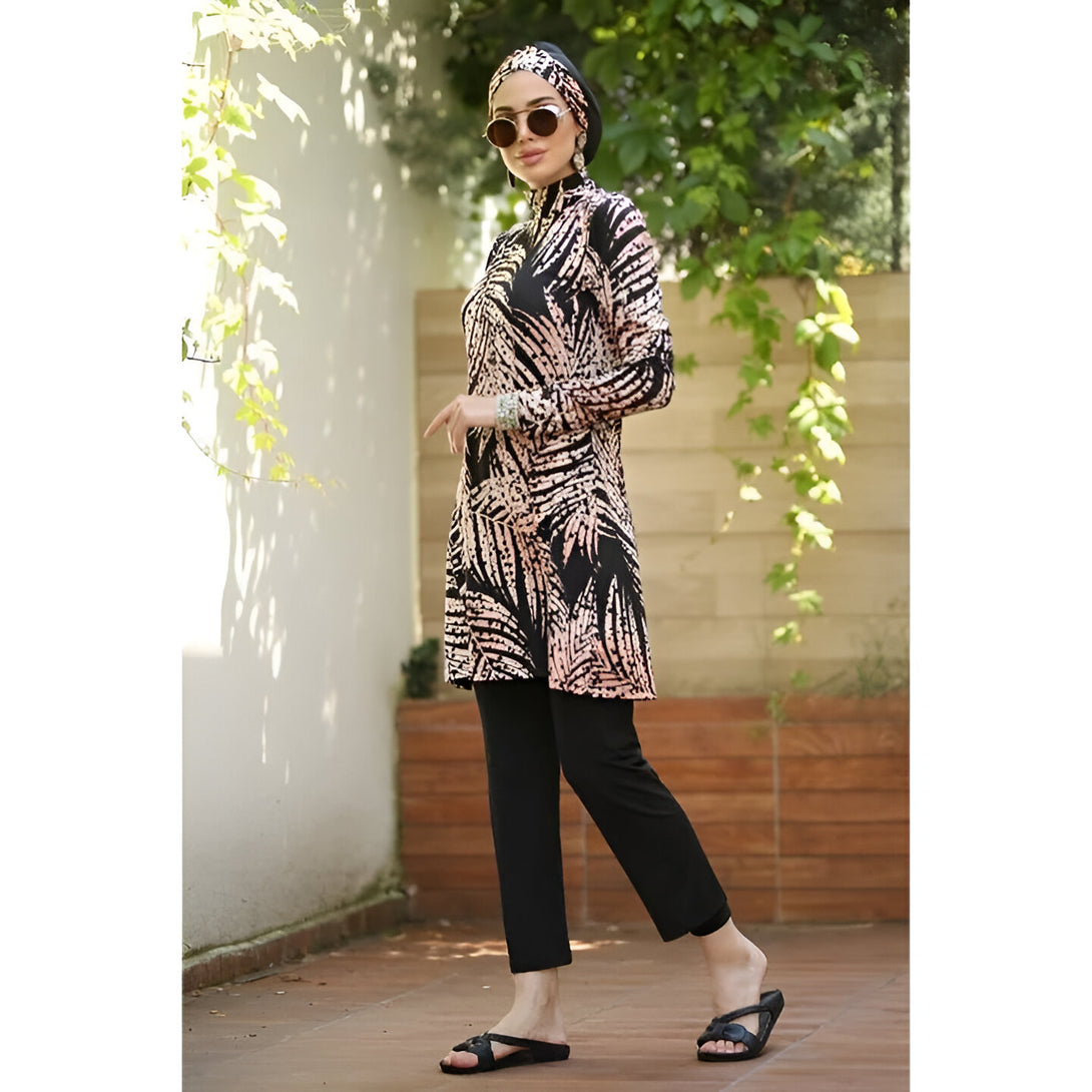 Une femme portant un maillot de bain musulman noir à imprimé floral avec un hijab noir et des lunettes de soleil. Elle porte également un pantalon noir et des sandales.