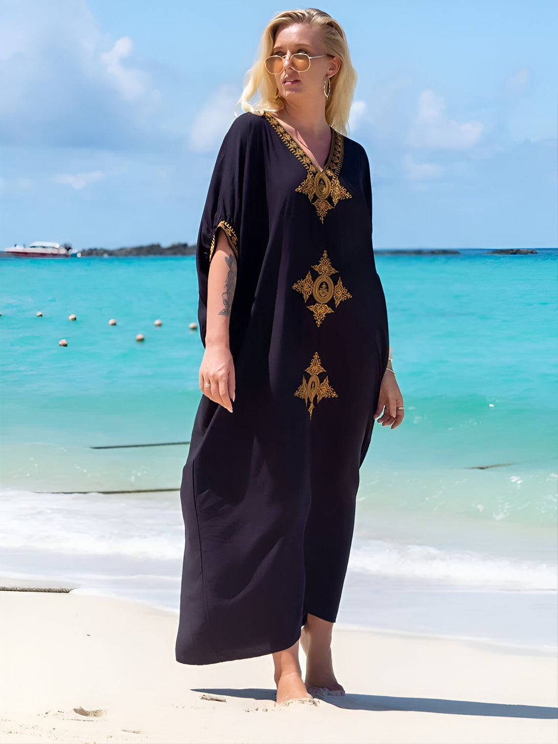 Une femme portant une longue robe noire à manches courtes et brodée d'or sur la plage. La robe est élégante et parfaite pour les occasions spéciales ou le quotidien.