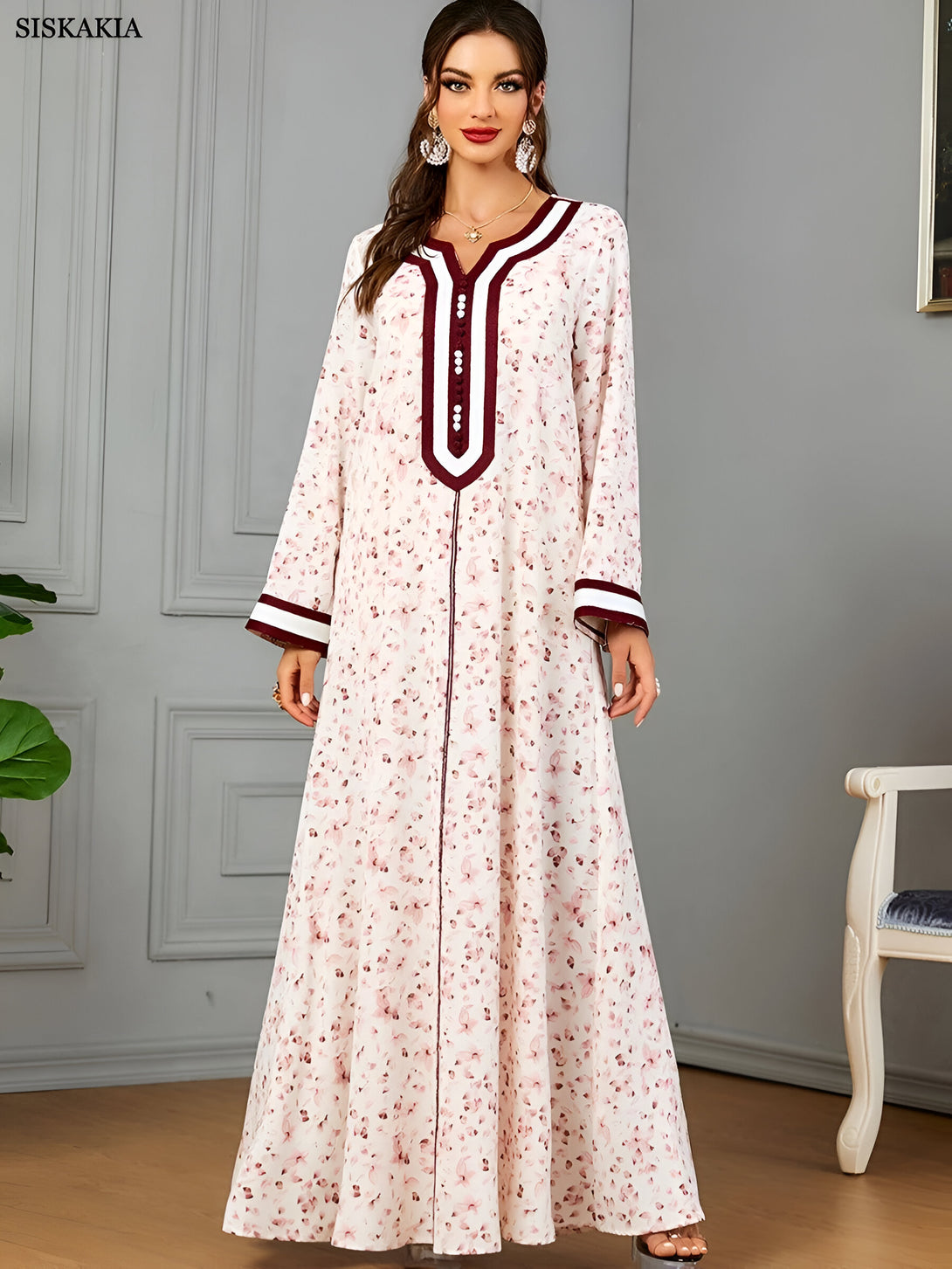 Une femme portant une longue robe blanche à fleurs avec des détails bordeaux et blancs. La robe a des manches longues et une encolure en V.
