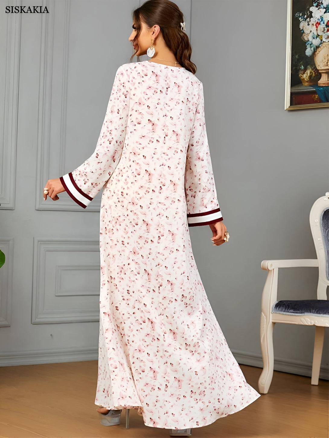 Une femme porte une longue robe blanche à fleurs avec des manches longues et une bordure rouge. La robe est ample et fluide, parfaite pour les occasions spéciales.