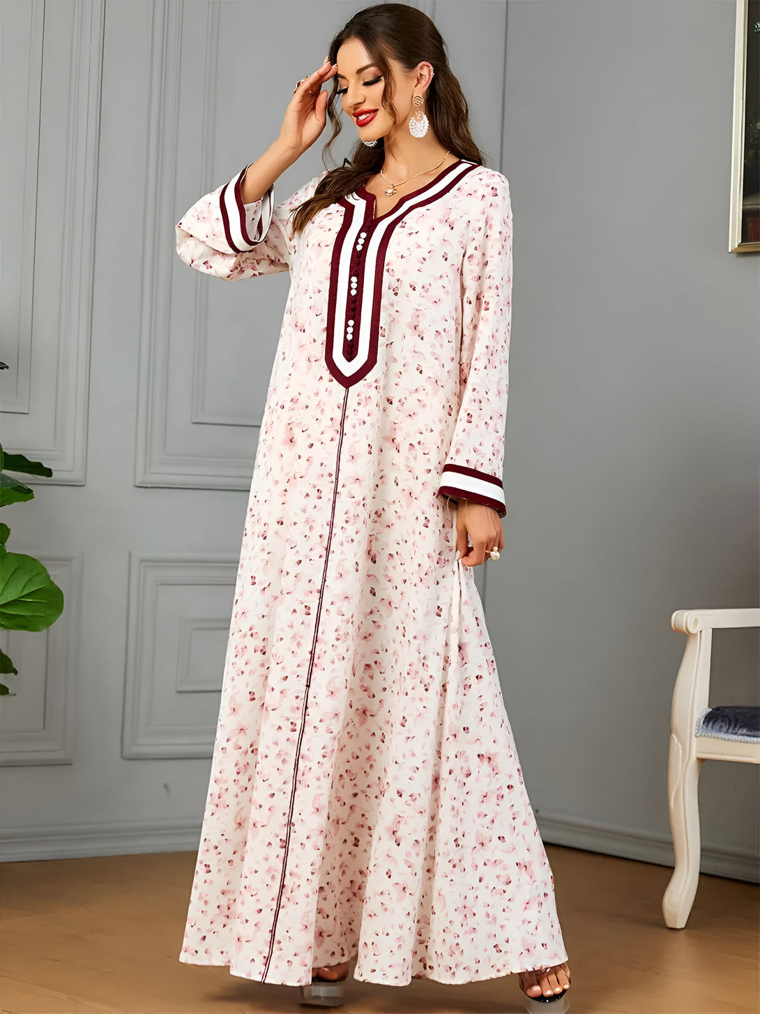 Une femme porte une longue robe blanche à fleurs avec des détails bordeaux. La robe a des manches longues et une encolure en V. Elle est parfaite pour les occasions spéciales ou pour tous les jours.