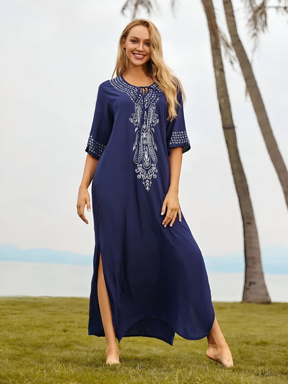 Une femme souriante porte une robe longue bleu marine avec des broderies blanches. La robe est élégante et confortable, parfaite pour les occasions spéciales ou les sorties décontractées.