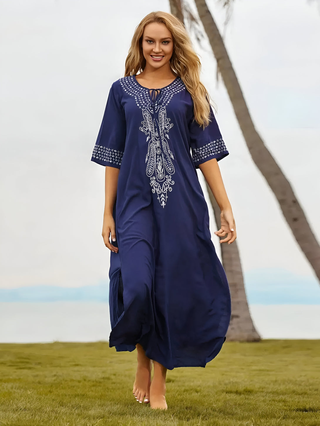 Une femme portant une robe bleue longue avec des broderies blanches. La robe est ample et flottante, idéale pour les journées chaudes.