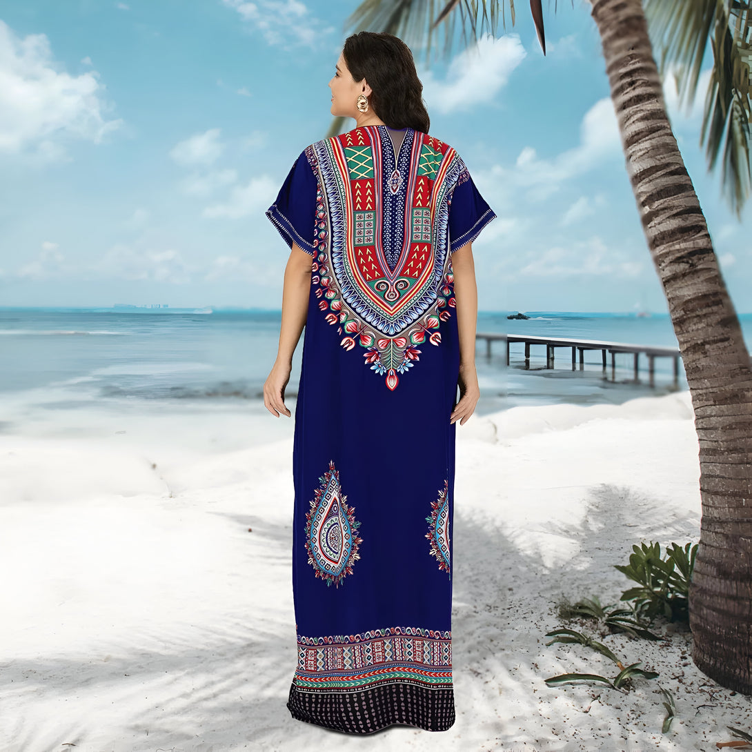 Une femme portant une longue robe bleue à imprimé africain, debout sur une plage de sable blanc. La robe a des motifs multicolores et est parfaite pour les occasions spéciales ou décontractées.