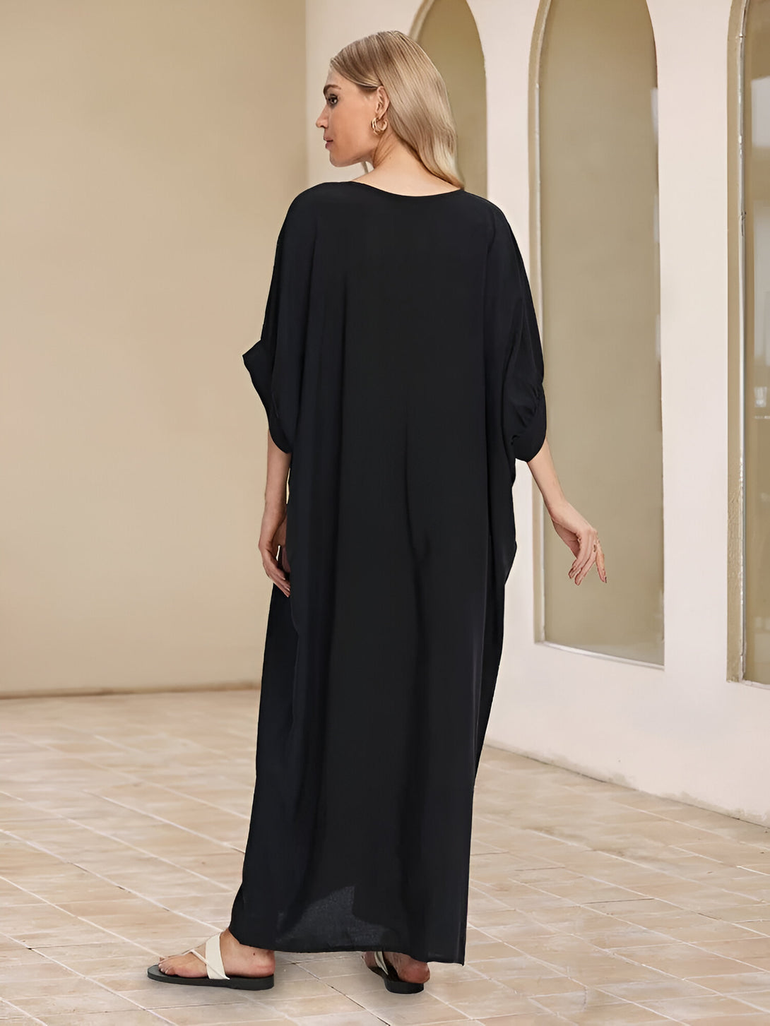Une femme portant une longue robe noire ample de style musulman. La robe a des manches courtes et une encolure ronde. La femme porte des sandales blanches.