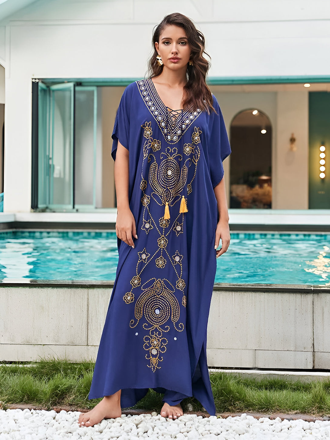 Une femme portant une longue robe bleue à manches courtes avec des motifs dorés et des franges jaunes. La robe est ornée de détails complexes et élégants.