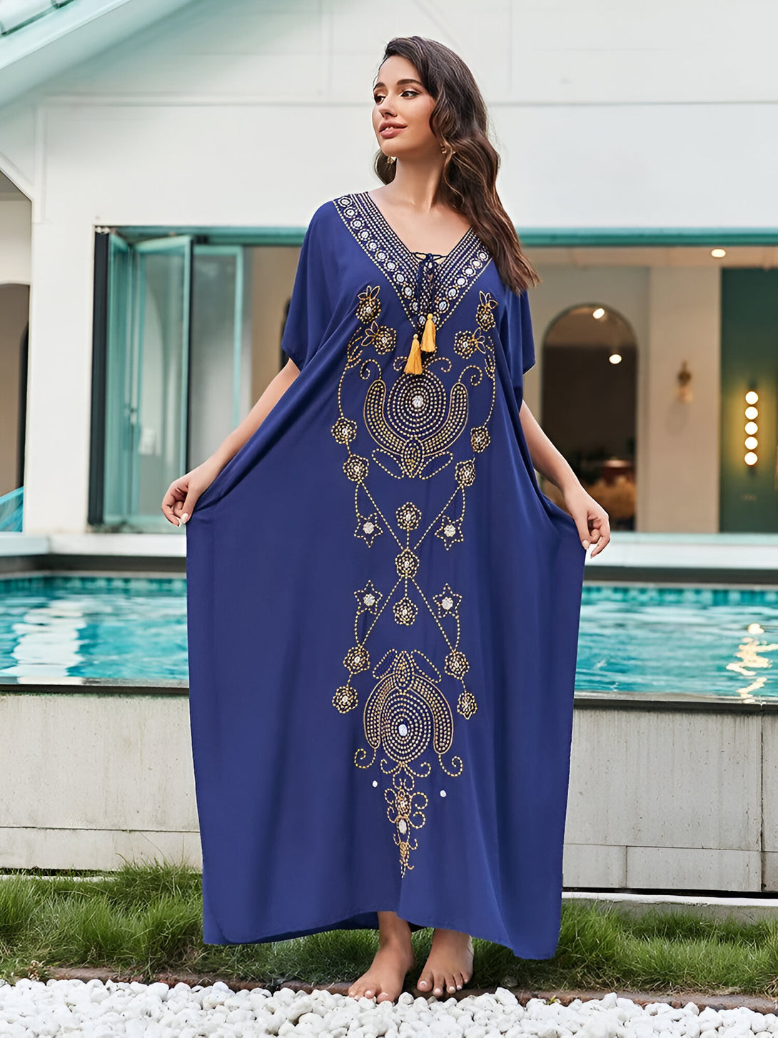 Une femme porte une robe longue bleu marine avec des motifs dorés. La robe est ample et fluide, et elle a un décolleté en V. La femme a l'air élégante et confortable.