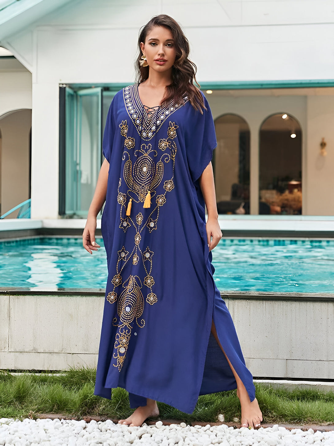 Une femme porte une longue robe bleue avec des détails dorés et des glands. La robe est ample et flottante, parfaite pour les occasions décontractées ou formelles. Elle est idéale pour les femmes musulmanes qui cherchent une tenue élégante et modeste.