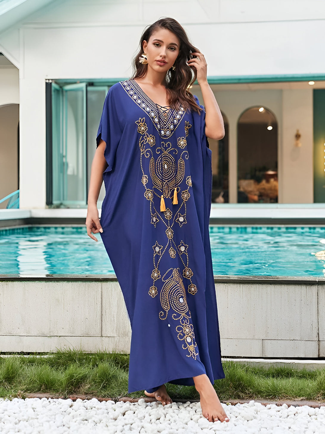 Une femme portant une robe longue bleue avec des motifs dorés et des glands. La robe est parfaite pour les occasions spéciales ou pour se détendre à la maison.