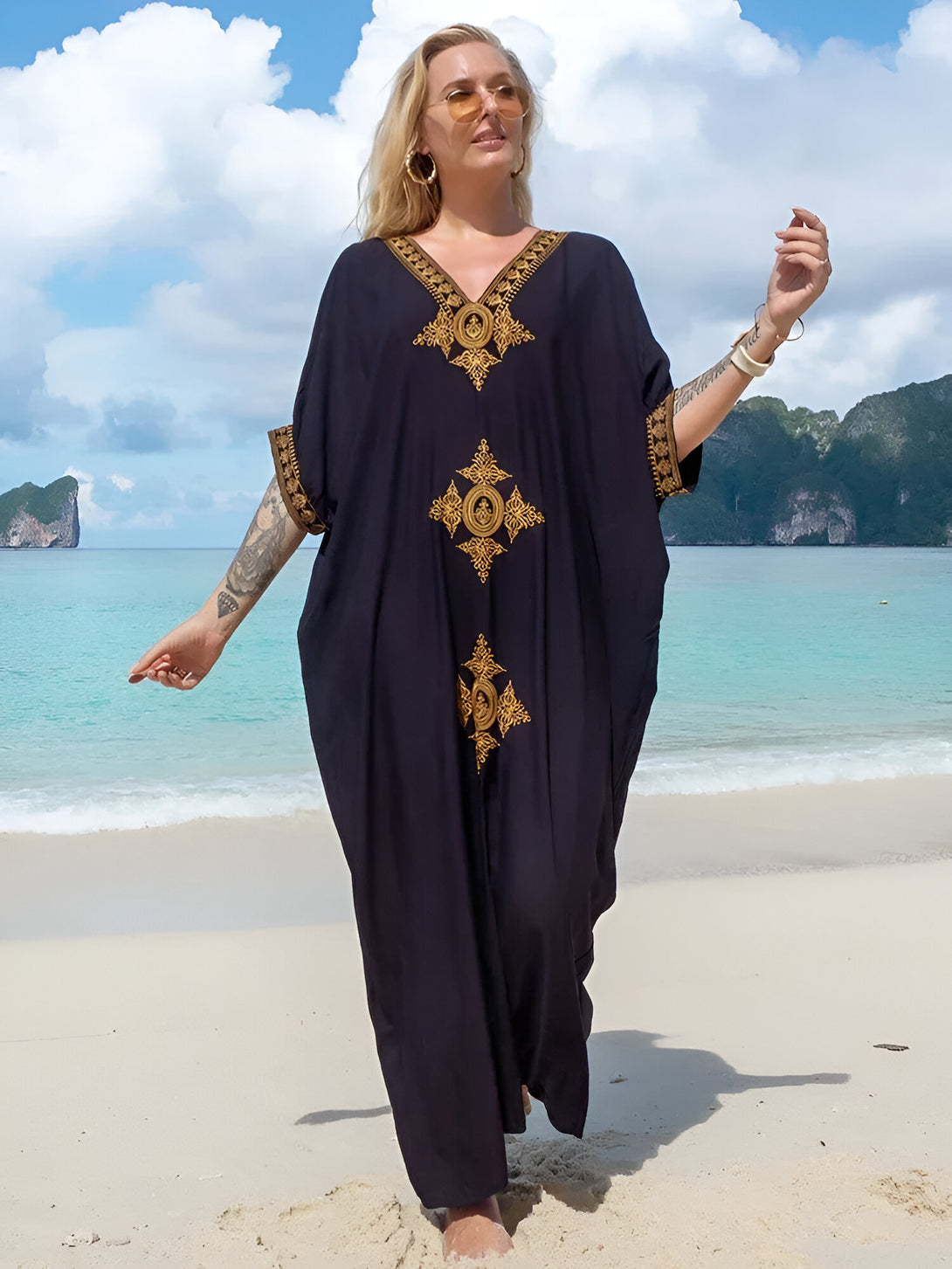 Une femme portant une longue robe noire avec des broderies dorées sur la plage. La robe est ample et confortable, idéale pour les journées chaudes.