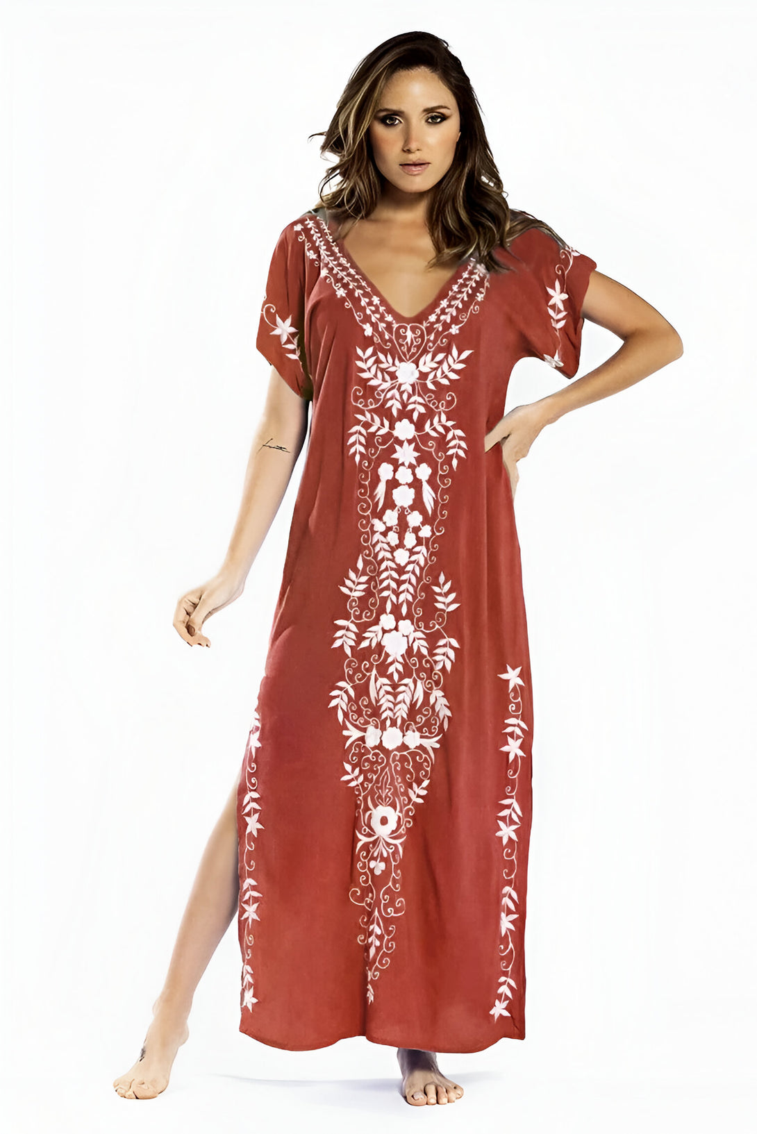 Une femme porte une longue robe rouge avec des motifs floraux brodés en blanc. La robe est ample et a des manches courtes. La robe est parfaite pour les occasions spéciales ou pour un look décontracté.