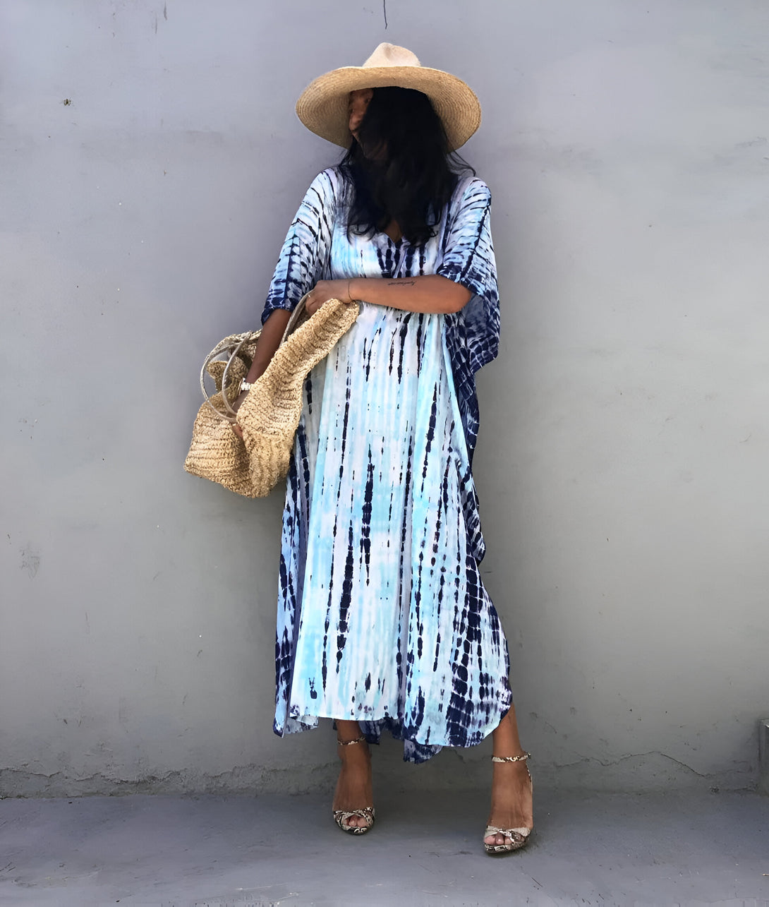 Une femme portant une robe longue bleu et blanche à motifs tie-dye, un chapeau de paille et des sandales à talons. Elle tient un panier en osier. Vêtements musulmans.
