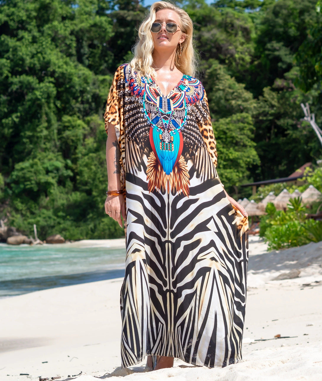 Une femme portant une robe longue musulmane à imprimé zèbre sur la plage. La robe est de couleur blanche et noire avec un col en V et des manches courtes. La femme porte également des lunettes de soleil.
