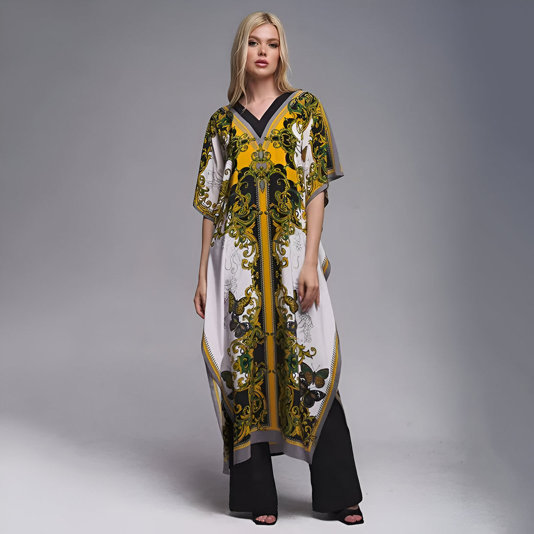 Une femme portant une longue robe blanche à manches courtes avec un imprimé jaune et noir. La robe est ornée de motifs floraux et de papillons. La femme porte également des pantalons noirs.