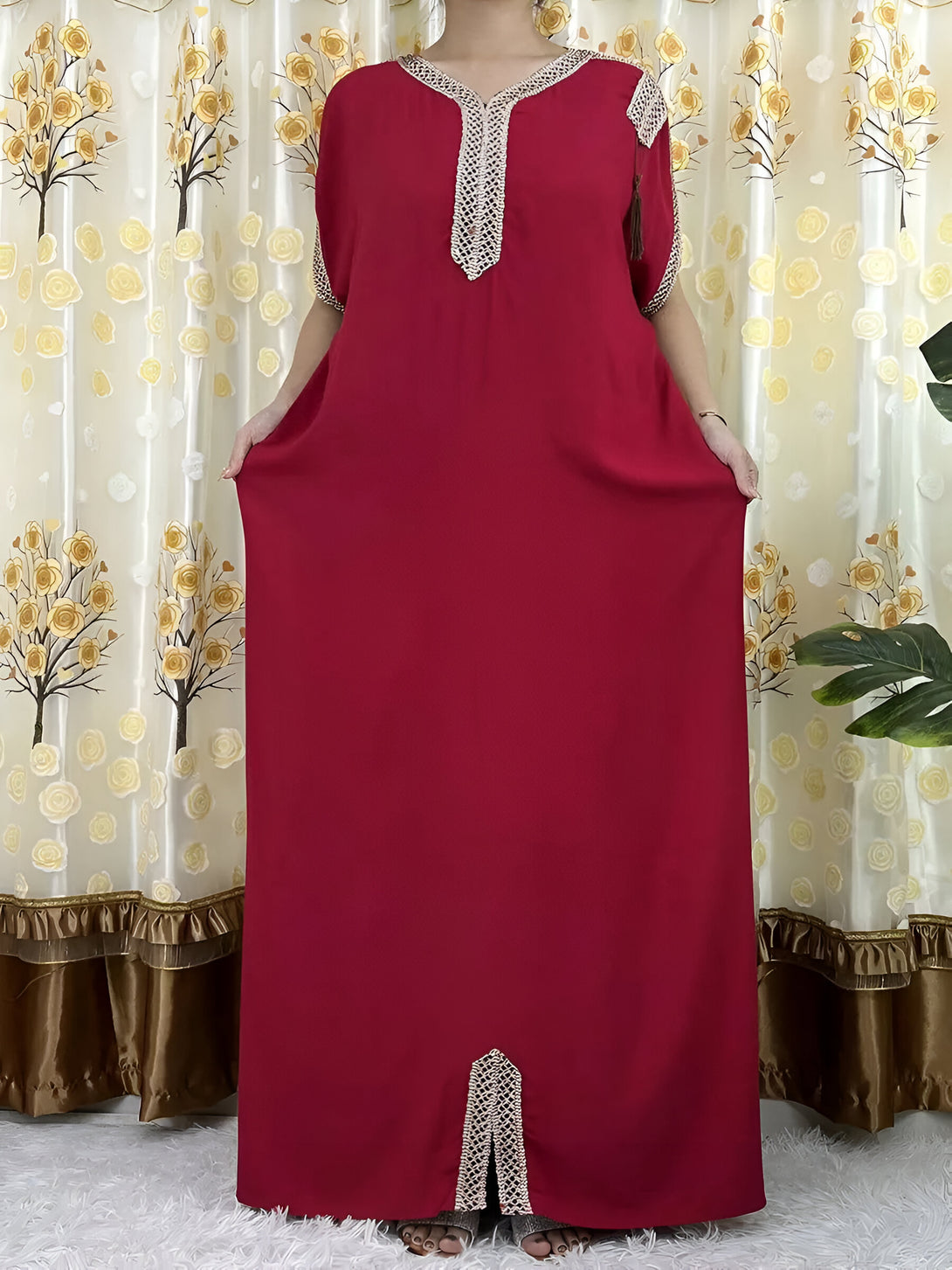 Robe longue rouge pour femmes musulmanes avec des détails de dentelle dorée. La robe a un col en V et des manches courtes. Elle est parfaite pour les occasions spéciales ou pour un look quotidien élégant.