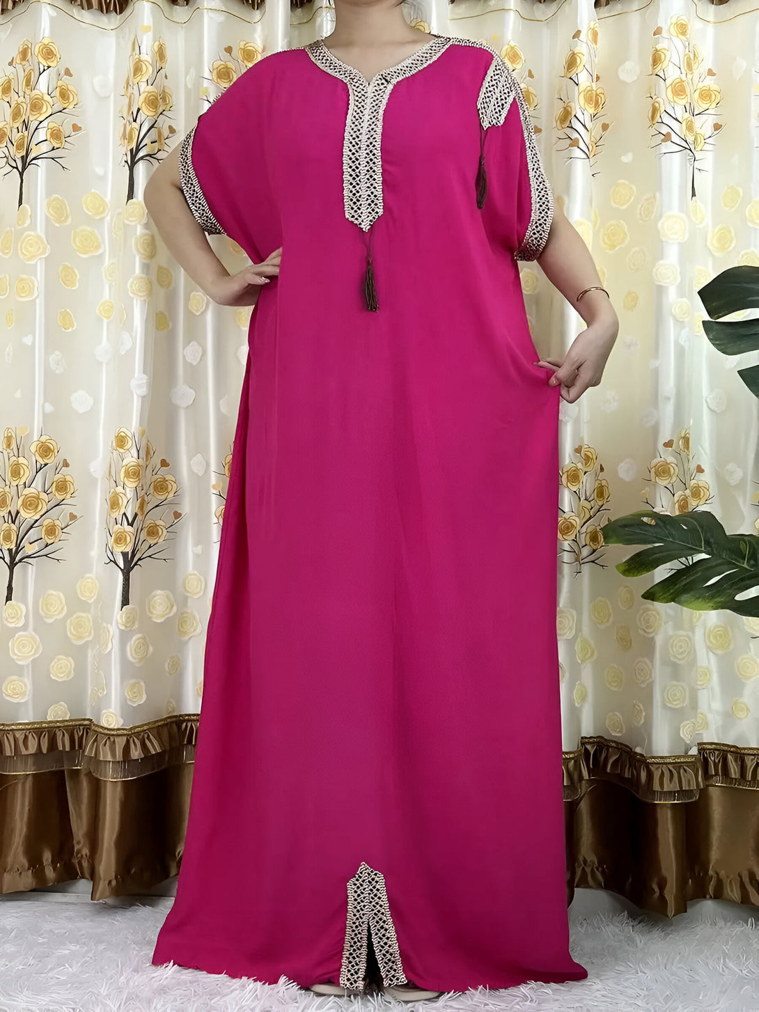 Une robe longue rose pour femme musulmane avec des détails dorés et une fente sur le devant. La robe est faite d'un tissu léger et fluide.