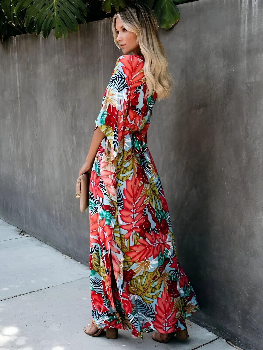 Une femme porte une longue robe à fleurs avec une ceinture à la taille. La robe est de couleur rouge, bleue et verte avec un motif floral.