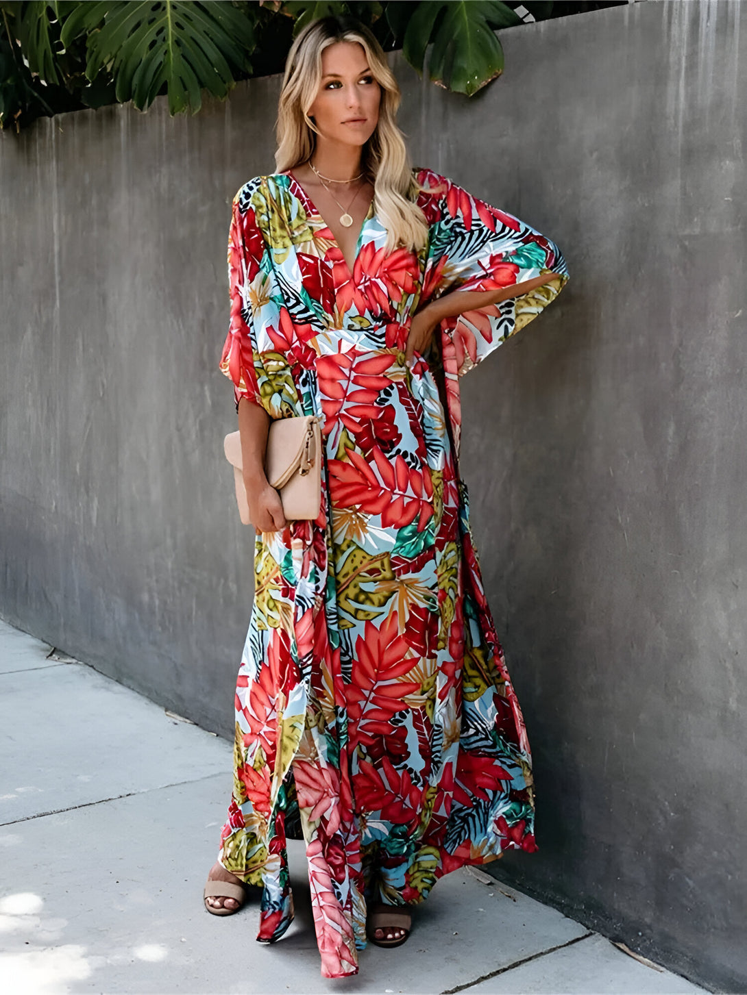 Une femme porte une longue robe ample à fleurs, idéale pour les occasions spéciales ou pour un look décontracté chic. La robe a un imprimé floral tropical et des manches 3/4.