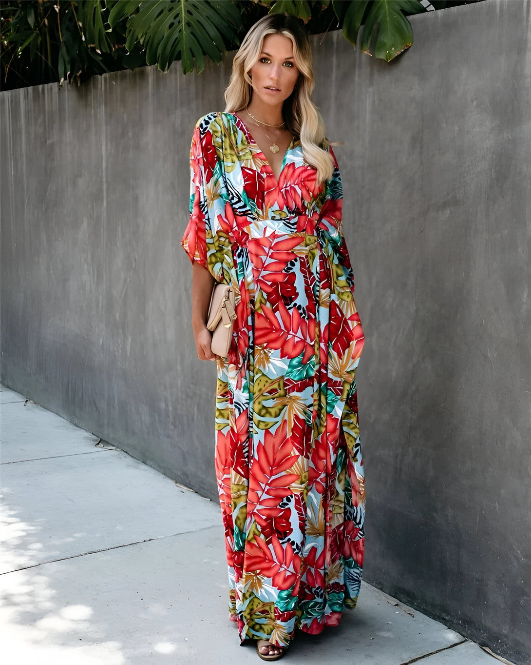 Une femme porte une longue robe à manches courtes avec un motif floral tropical. La robe est de couleur rouge, verte et bleue.