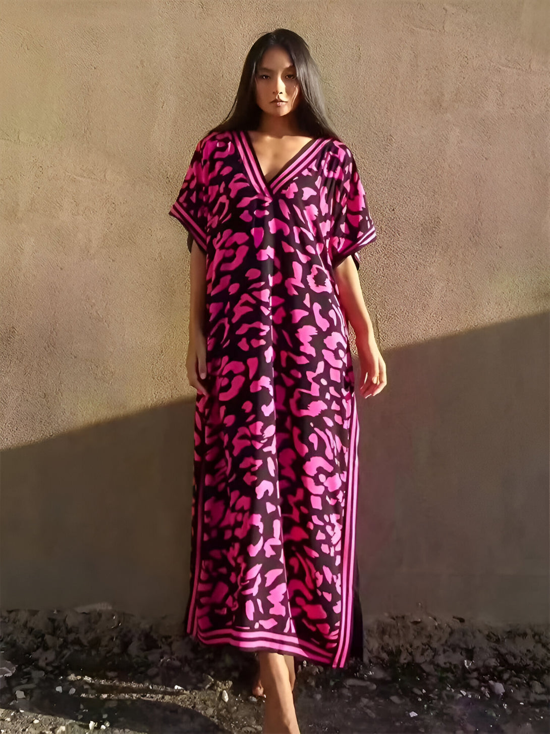 Une femme porte une longue robe rose à imprimé léopard avec des détails noirs. La robe a des manches courtes et un col en V.