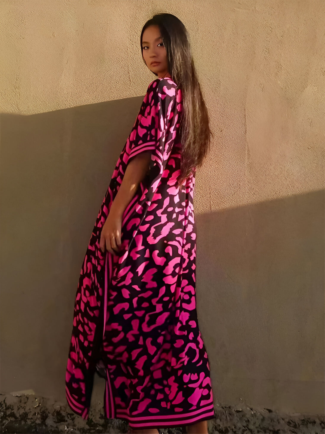 Une femme porte une longue robe rose à imprimé léopard. La robe a des manches courtes et une coupe ample.