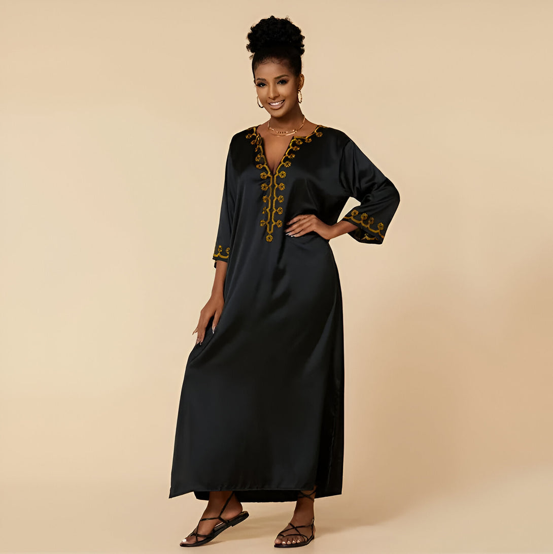 Une femme porte une robe longue noire élégante avec des broderies dorées. La robe a un col en V et des manches trois quarts. La robe est parfaite pour les occasions spéciales et les fêtes.