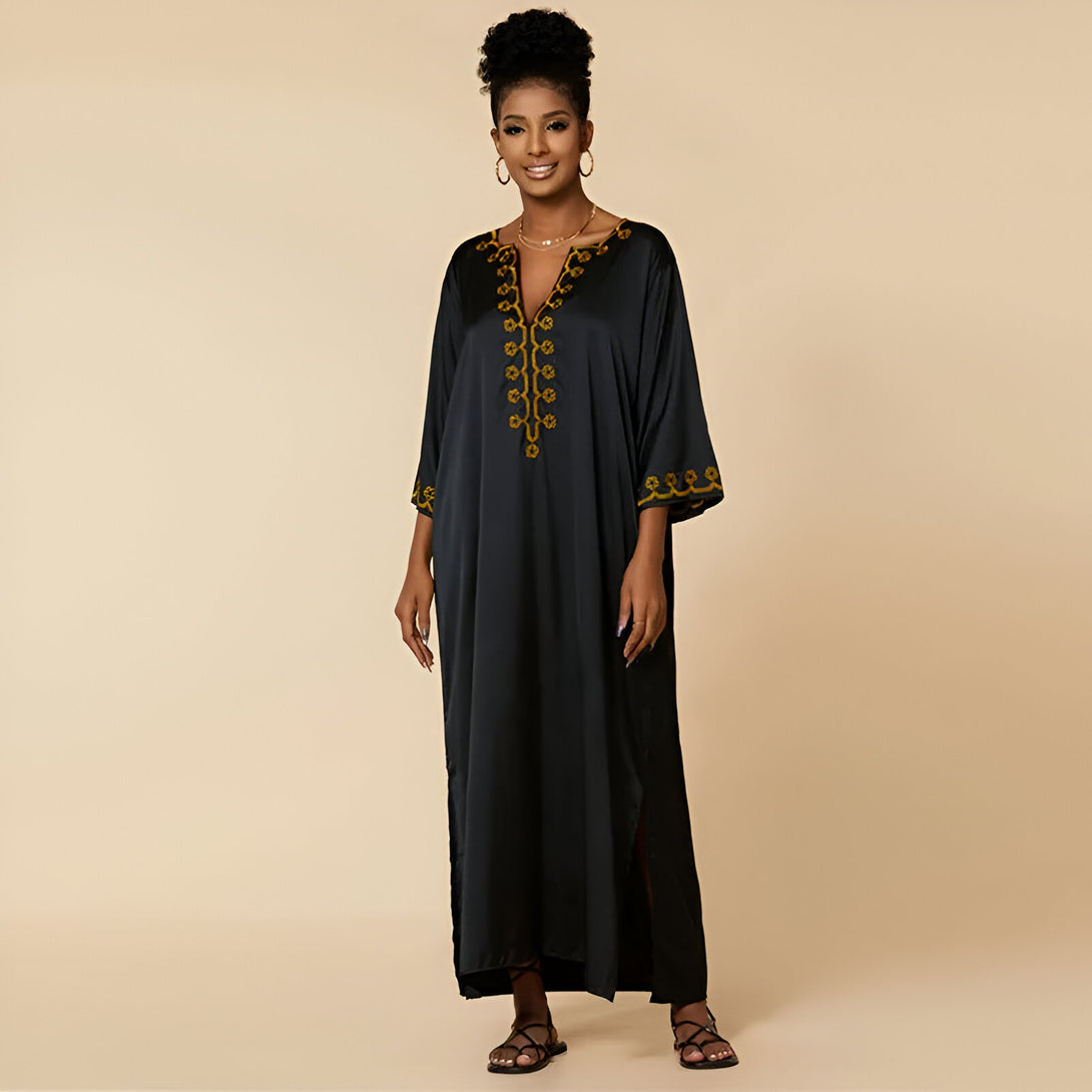 Une femme porte une longue robe noire en satin avec des broderies dorées. La robe a un col en V et des manches trois quarts.
