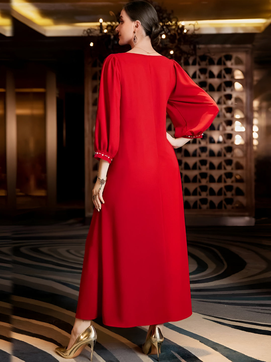 Une femme porte une robe rouge longue à manches bouffantes ornées de perles. La robe est ample et fluide, idéale pour une occasion spéciale.
