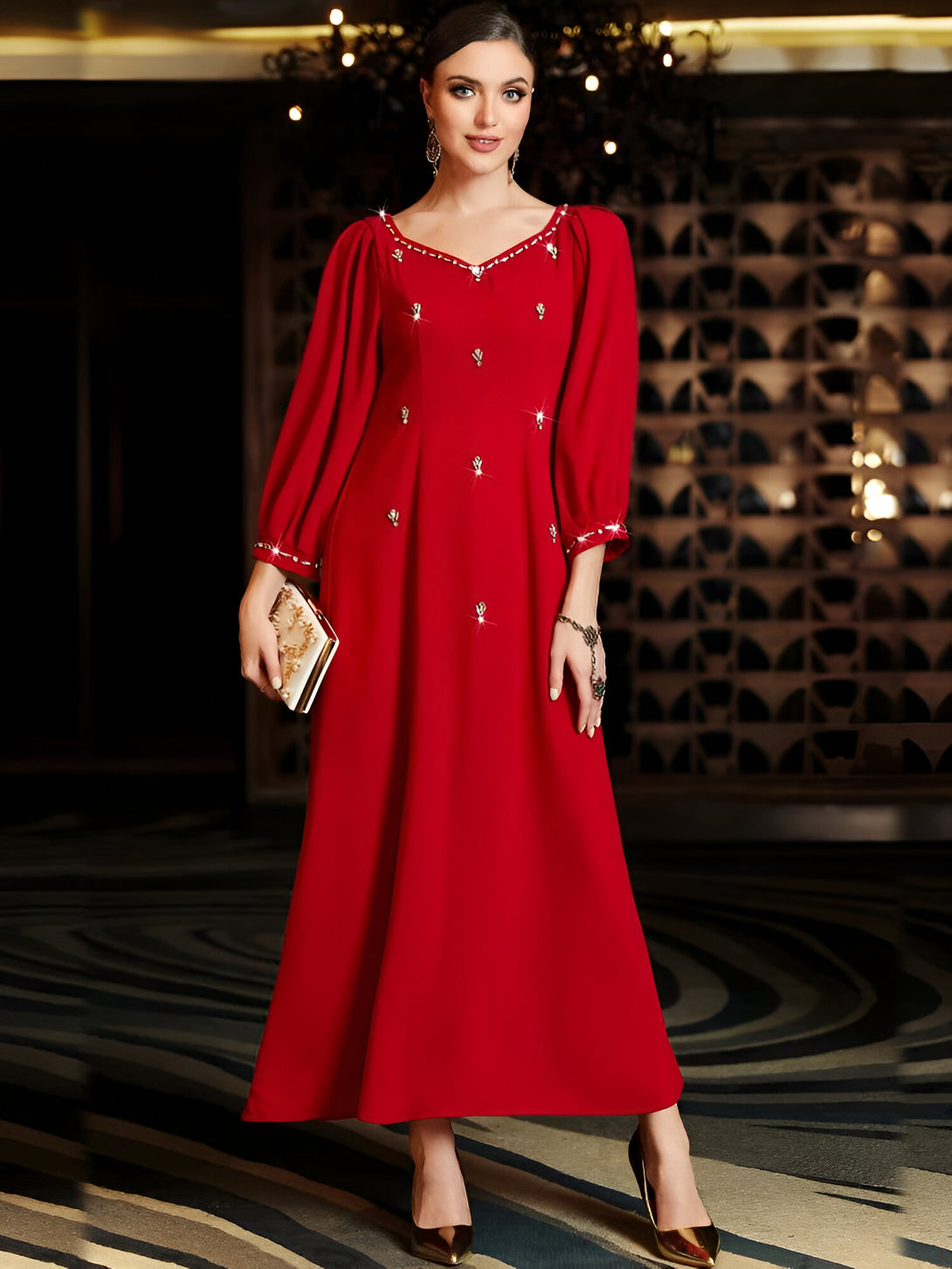 Une femme élégante porte une robe rouge longue avec des manches bouffantes et des détails de strass. La robe est idéale pour les occasions spéciales et les événements religieux.