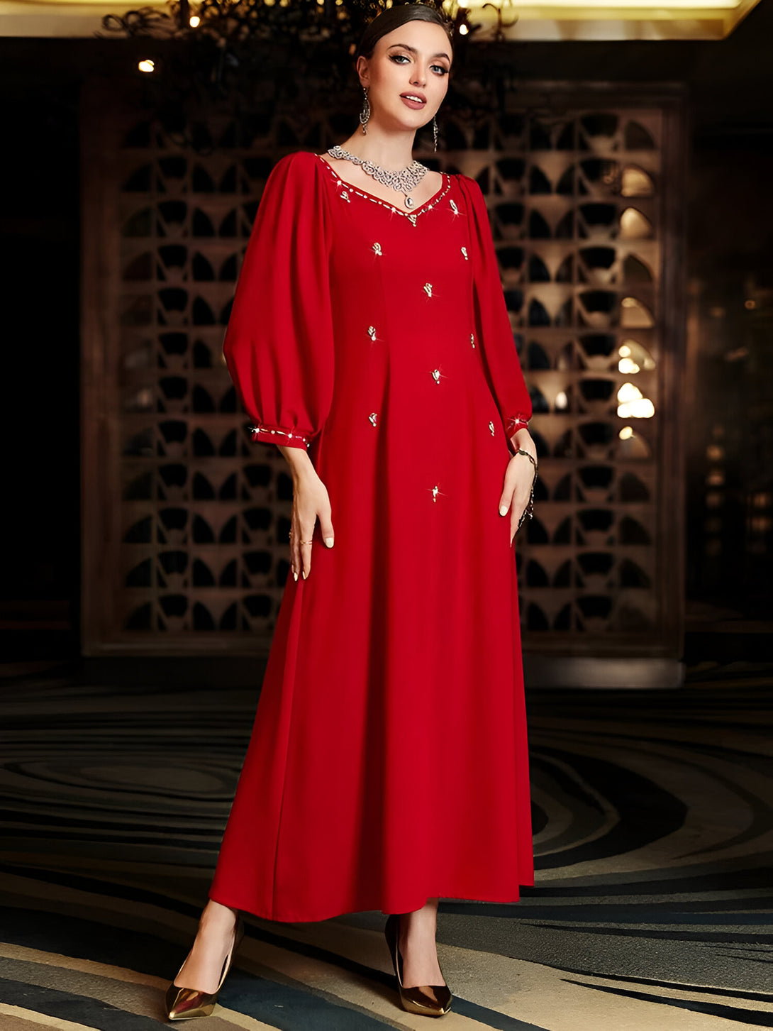 Une femme élégante portant une robe rouge longue avec des manches bouffantes ornées de strass. La robe est parfaite pour les occasions spéciales et les fêtes.