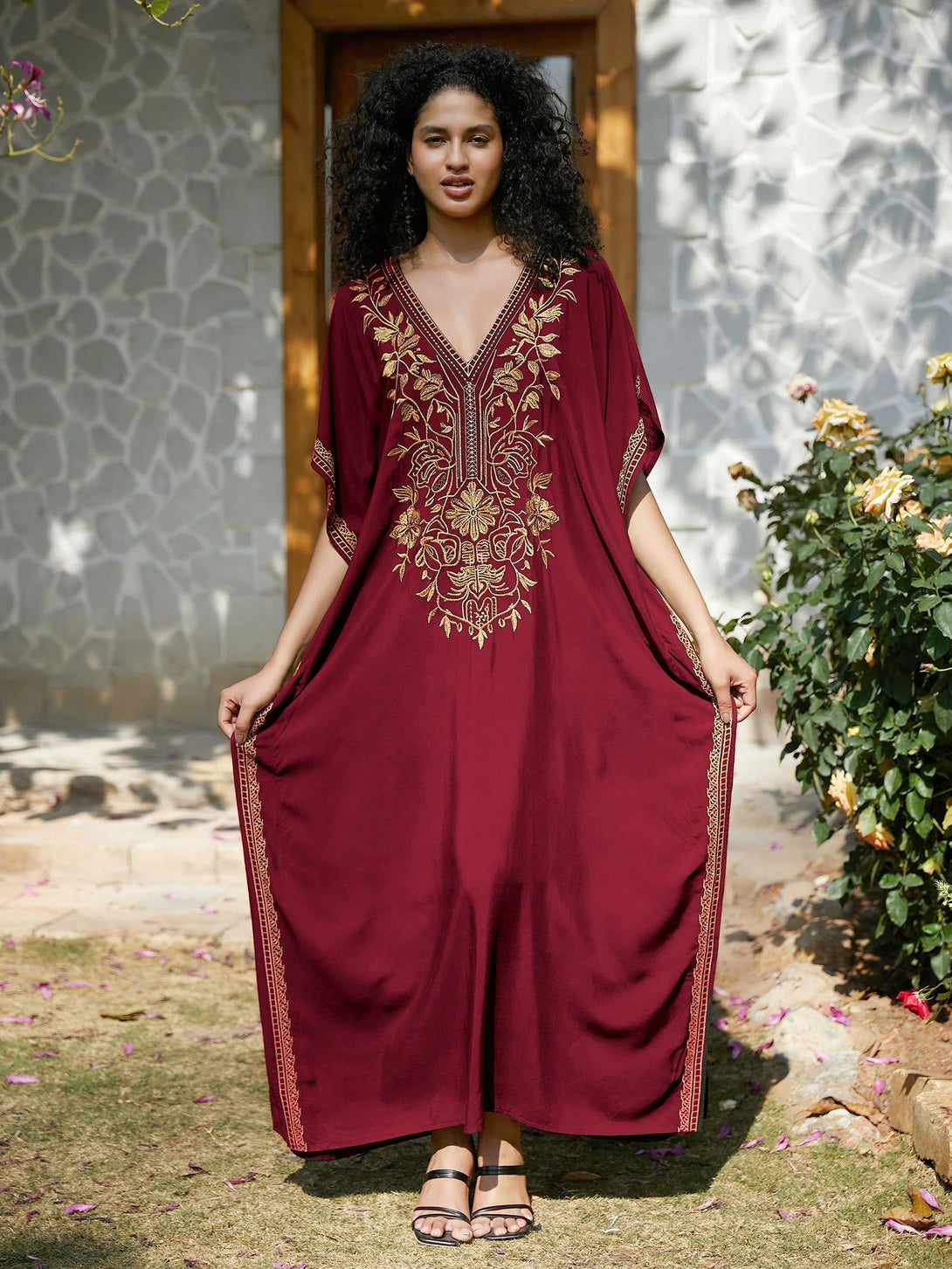 Une femme porte une longue robe bordeaux à manches courtes avec des broderies dorées. La robe est élégante et parfaite pour les occasions spéciales.