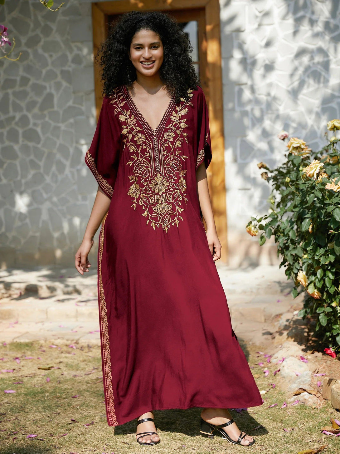 Une femme souriante porte une longue robe bordeaux à manches courtes, brodée de motifs dorés floraux. La robe est ample et fluide, parfaite pour les occasions spéciales.