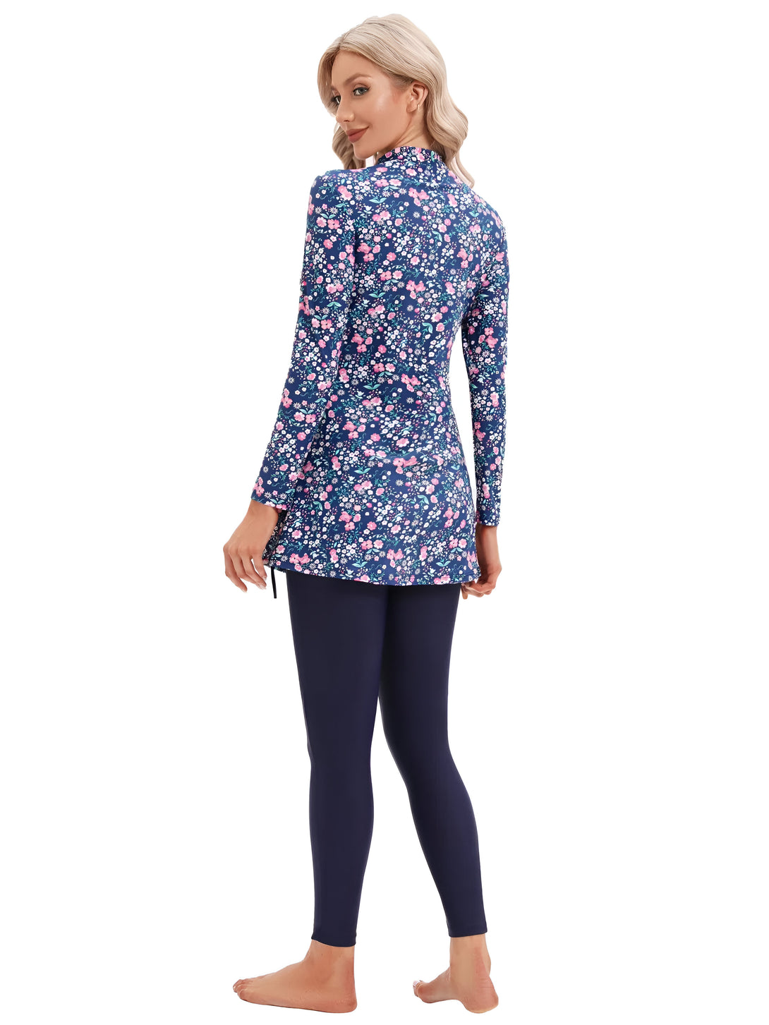 Une femme porte un maillot de bain musulman bleu marine à fleurs roses et blanches. Le maillot de bain est composé d'une tunique à manches longues et d'un legging assorti.