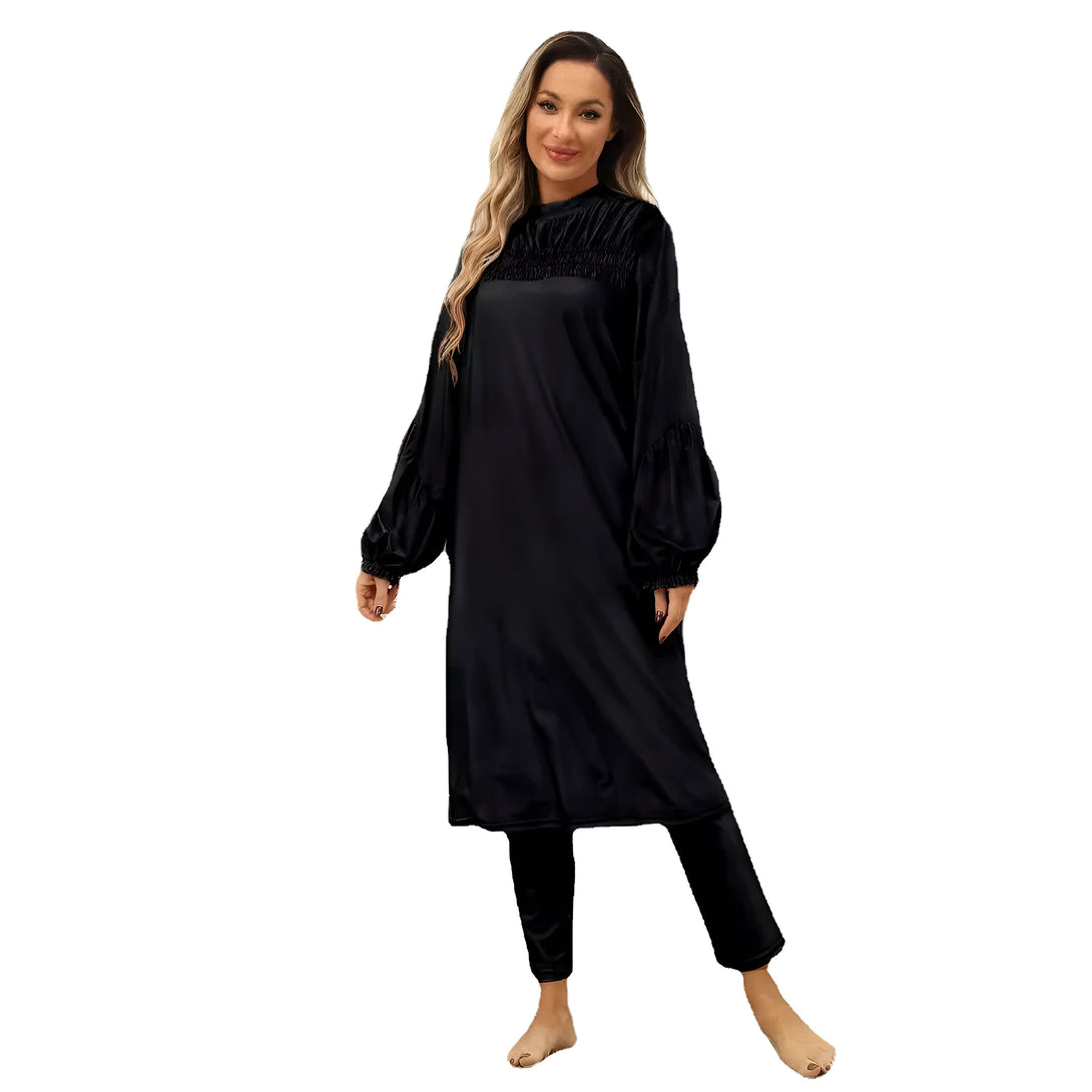 Une femme porte une robe noire à manches longues avec un pantalon assorti. La robe a un col rond et des manches bouffantes.