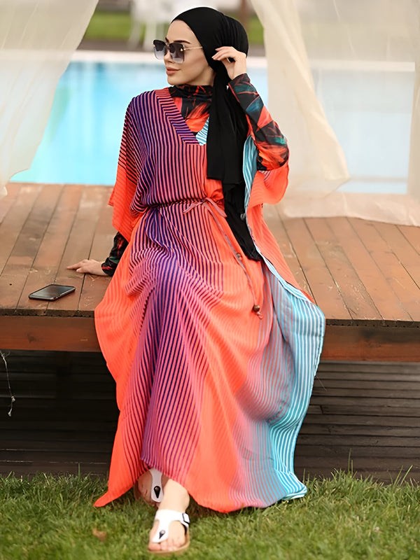 Une femme portant un hijab noir et une robe de plage rayée orange, bleue et violette. La robe est ornée d'une ceinture et a des manches longues. La femme porte des lunettes de soleil et est assise sur une terrasse en bois près d'une piscine.