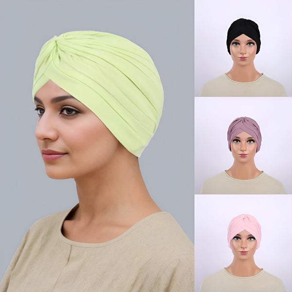 Une femme portant un turban en coton vert, un turban en coton noir, un turban en coton rose et un turban en coton mauve. Les turbans sont disponibles en plusieurs couleurs.