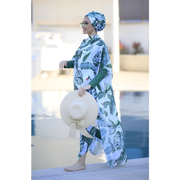 Une femme porte un maillot de bain musulman à motifs tropicaux avec un chapeau de paille et des lunettes de soleil. Elle se tient près d'une piscine.