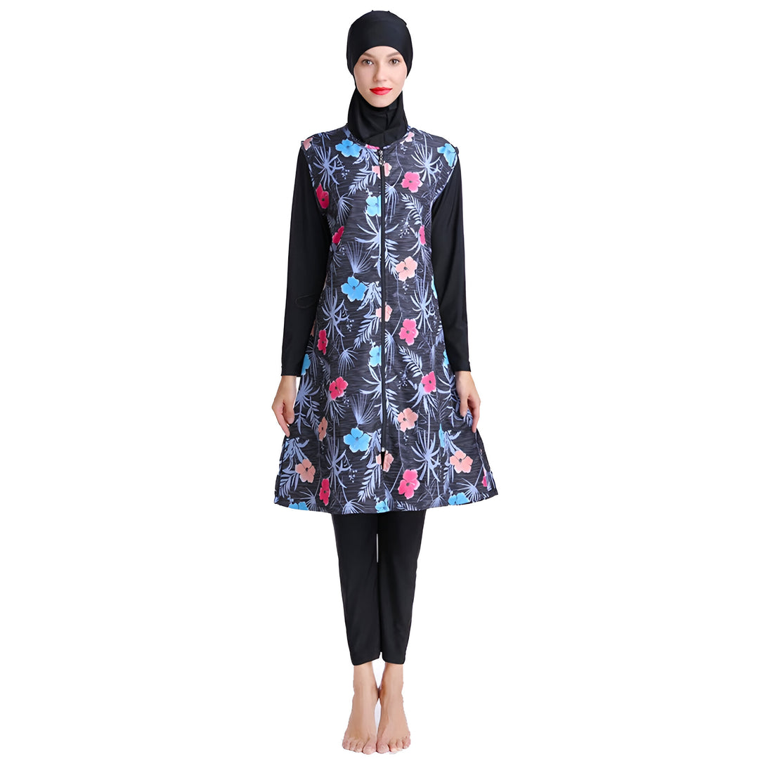 Une femme portant un maillot de bain musulman à manches longues avec un motif floral. Le maillot de bain est noir avec des fleurs bleues, roses et corail. La femme porte également un hijab noir.