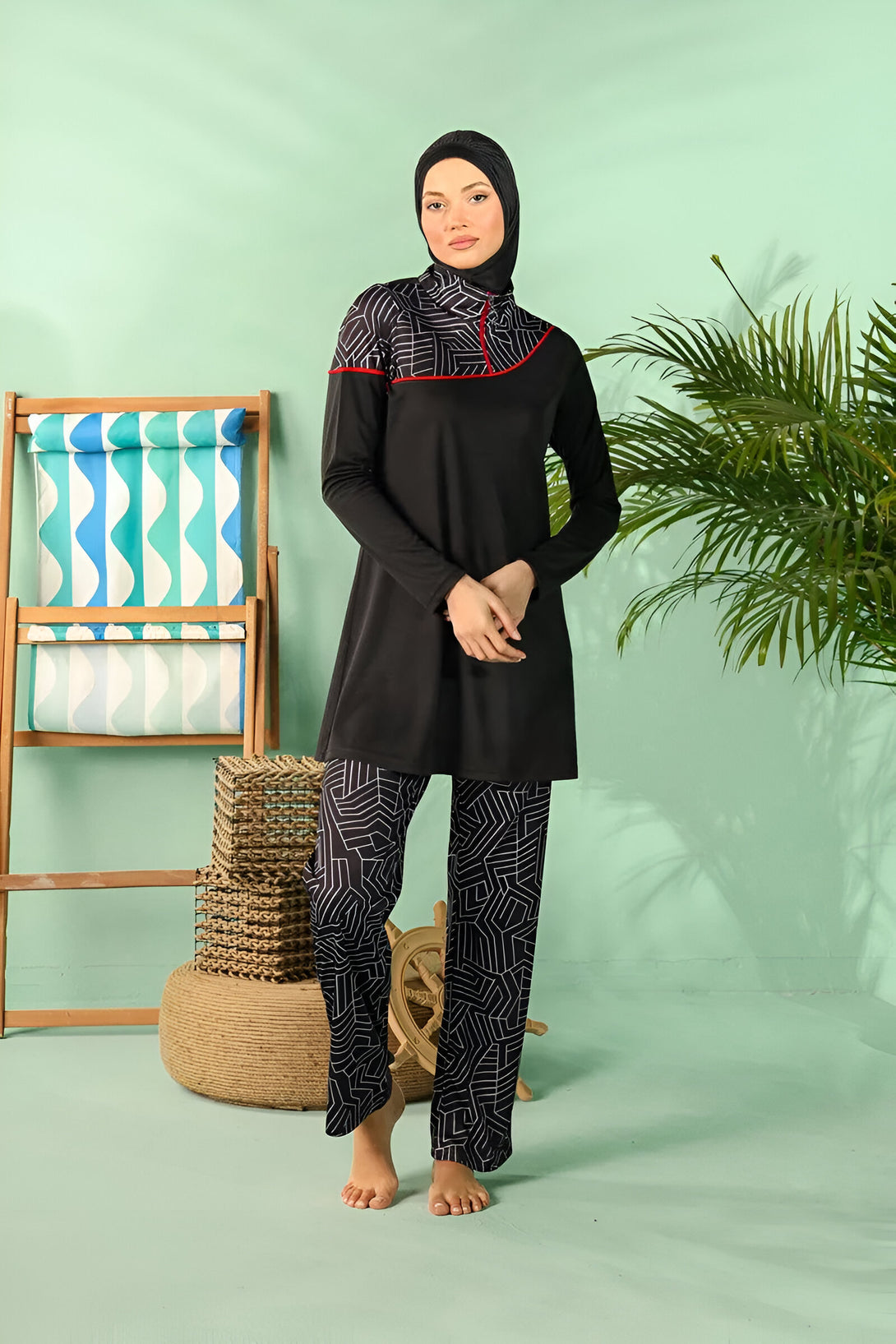 Une femme portant un maillot de bain musulman noir avec des détails blancs et une touche de rouge. Le maillot de bain est composé d'une tunique longue et d'un pantalon long. La femme est debout devant un fond vert et porte un hijab noir.