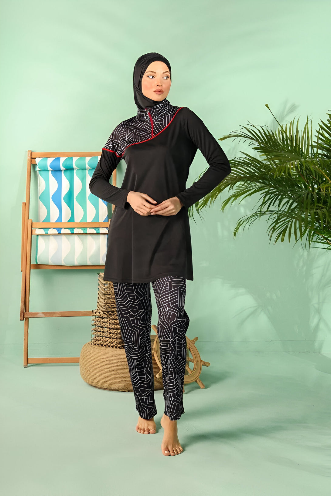 Une femme portant un maillot de bain musulman noir avec des motifs géométriques blancs. Le maillot de bain comprend une tunique à manches longues et un pantalon long. La femme est debout devant un fond vert.